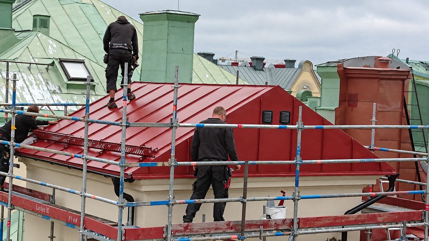 Plåtslagare lägger rött falsat plåttak på en stadsfastighet