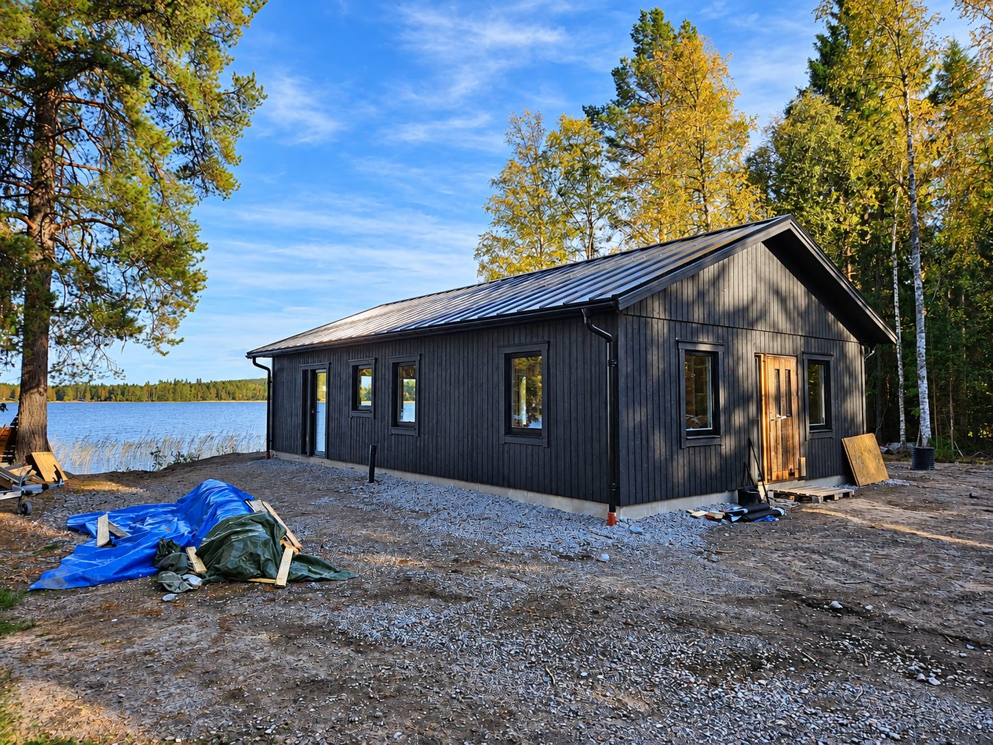 Färdigt svart trähus med plåttak vid sjön