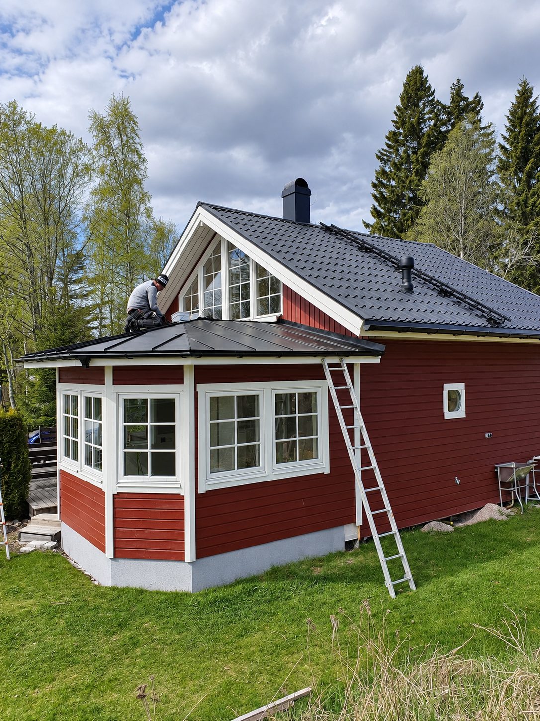 Plåtslagare lägger svart plåttak över glasverandan på en röd villa